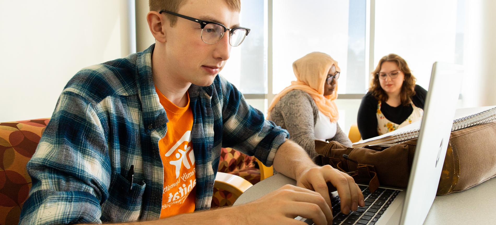 Guy on computer with 2 girls in background